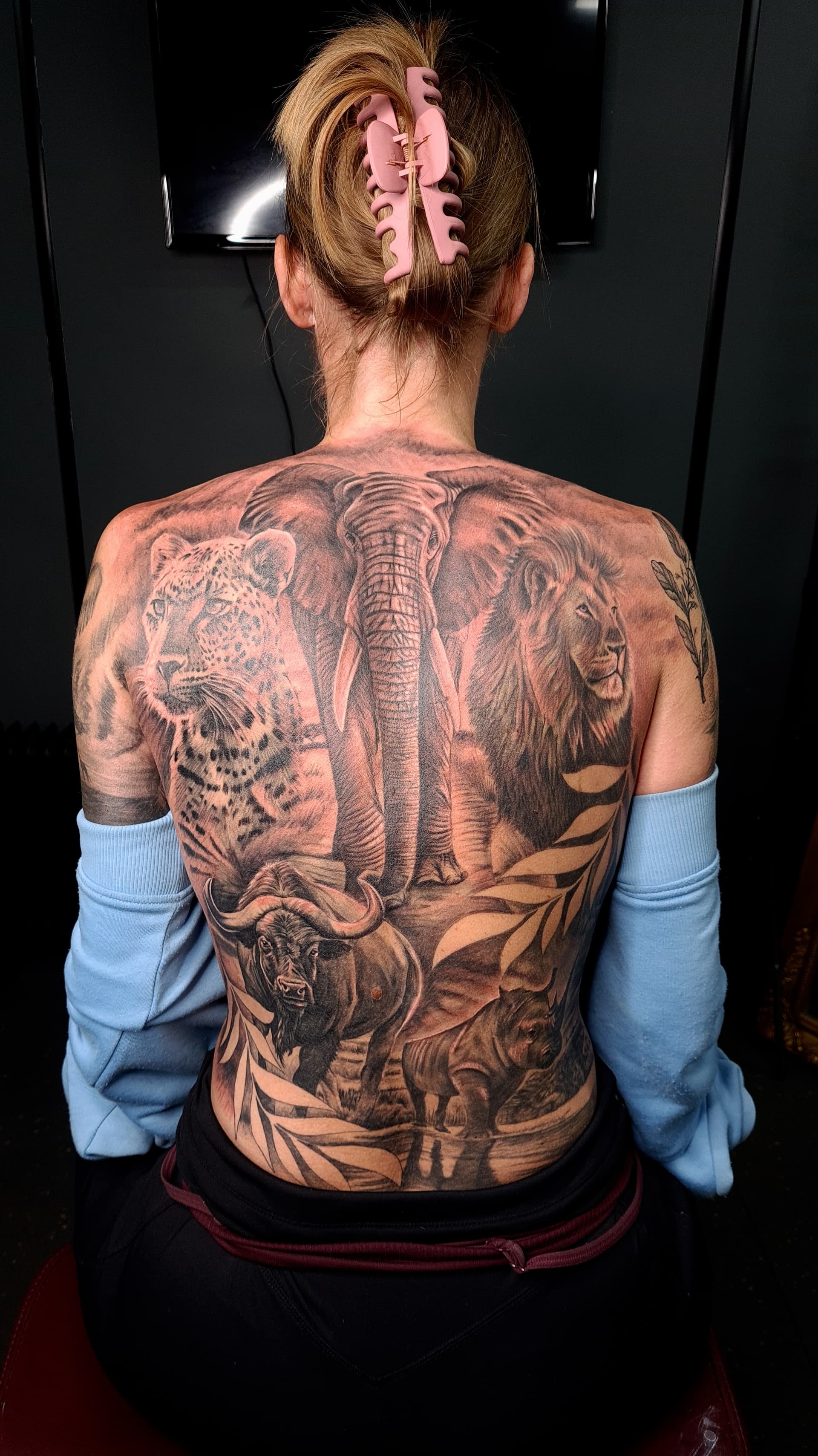 Back tattoo showcasing a lion, elephant, and leopard in black and grey realism style.
