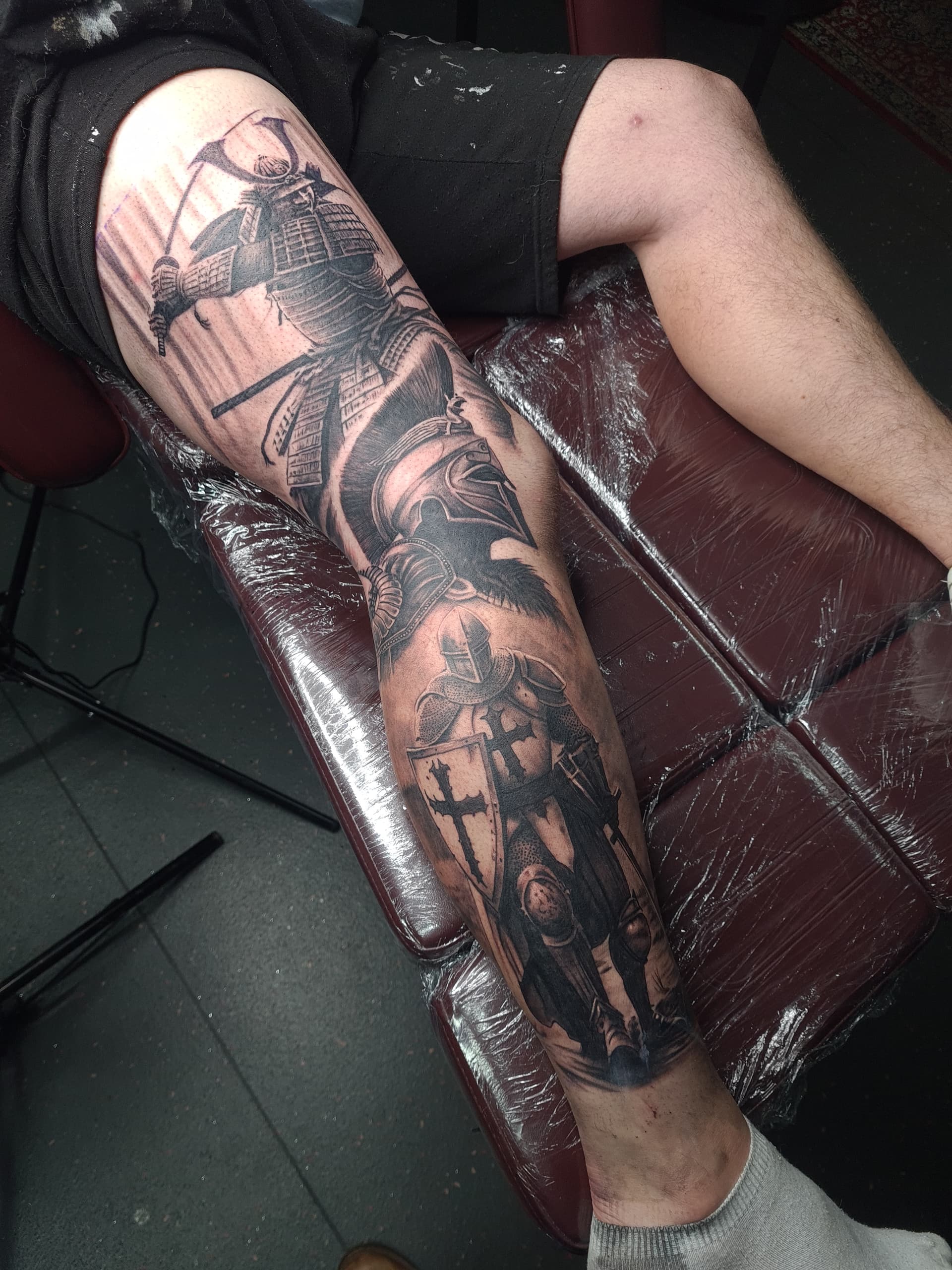 Detailed black and grey realism tattoo of a samurai and knight on leg.