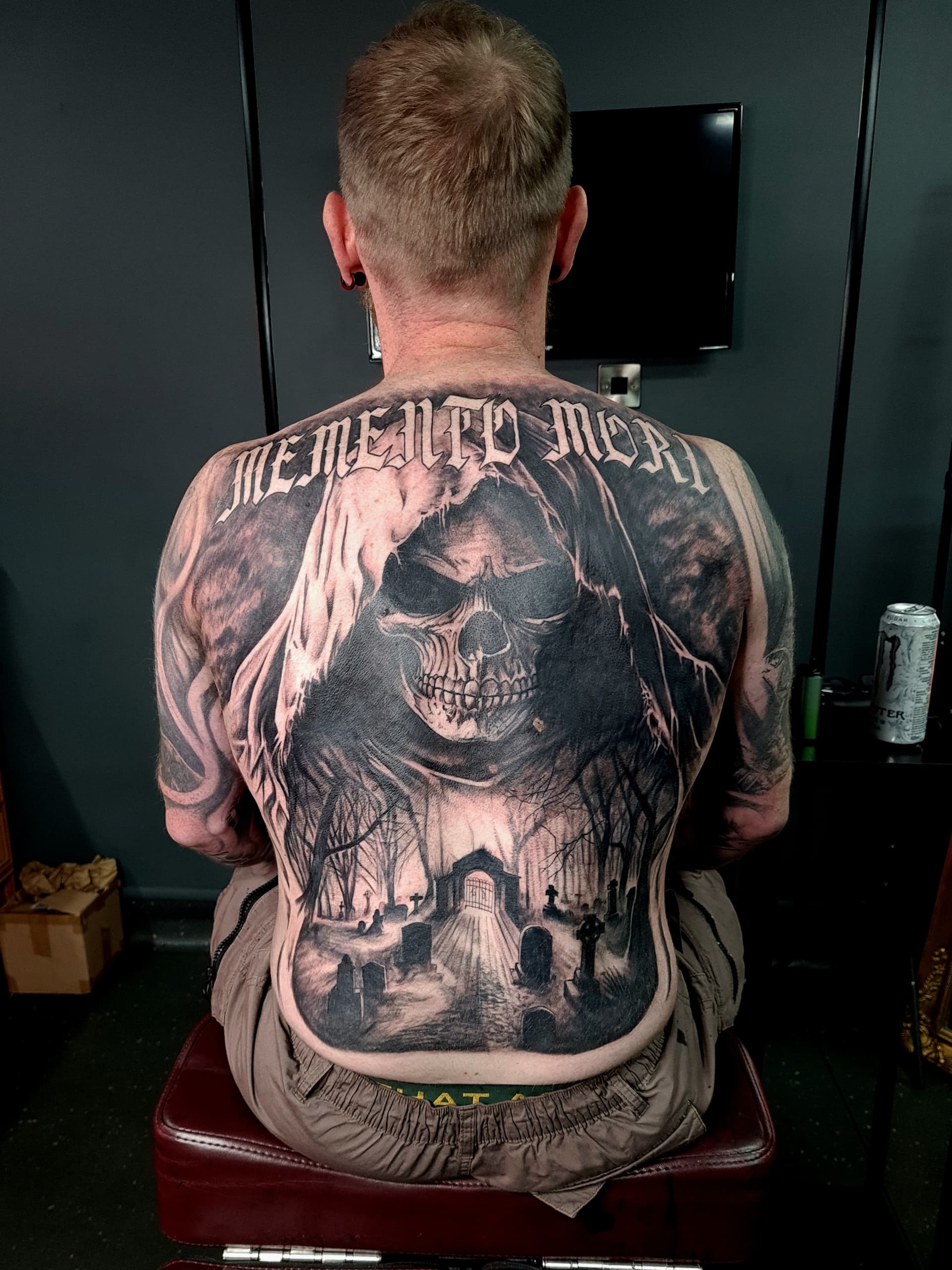 Detailed memento mori tattoo featuring a skull, graveyard, and trees on back.