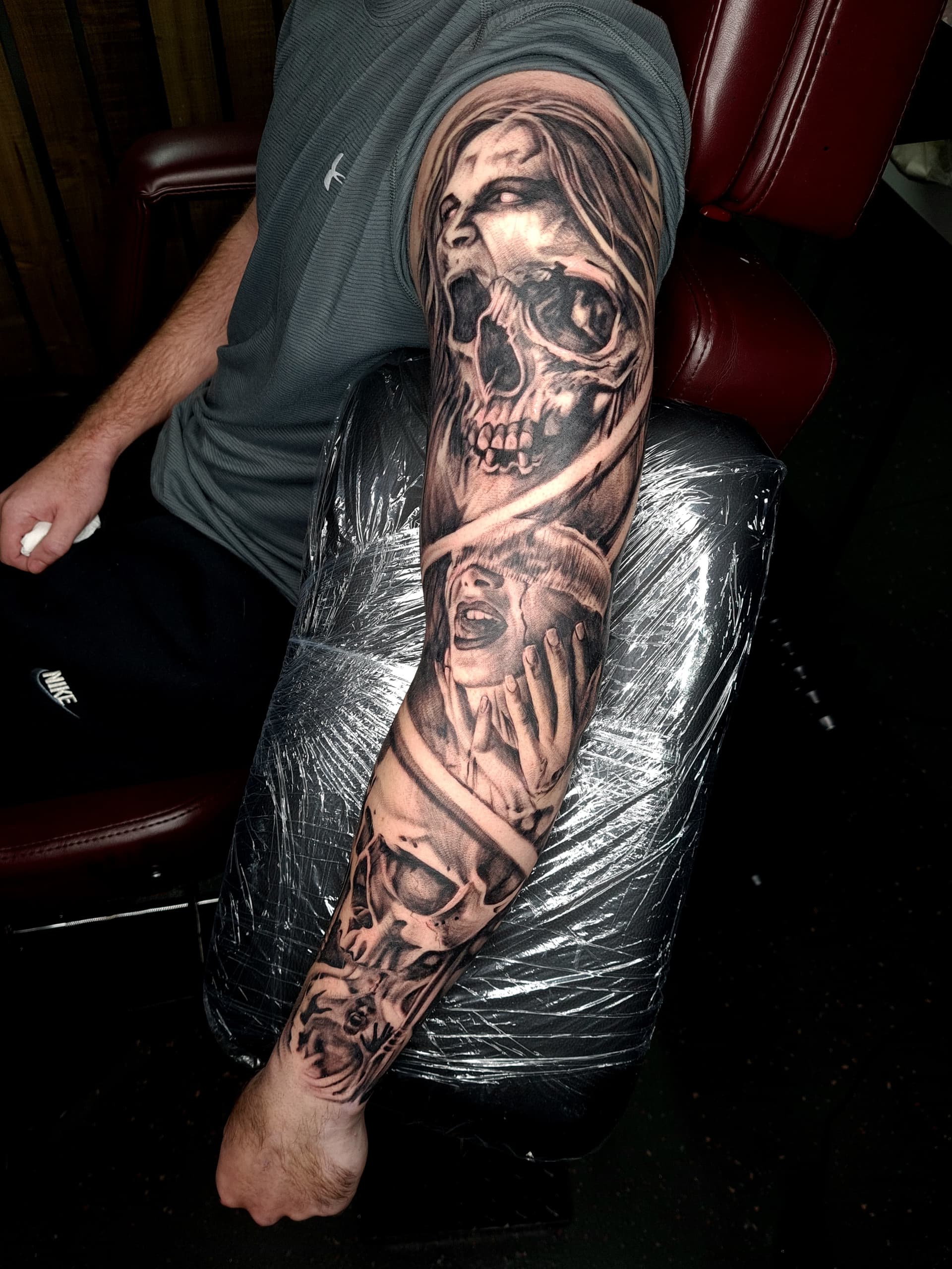 Detailed black and grey realism tattoo of skulls and screaming faces on arm.