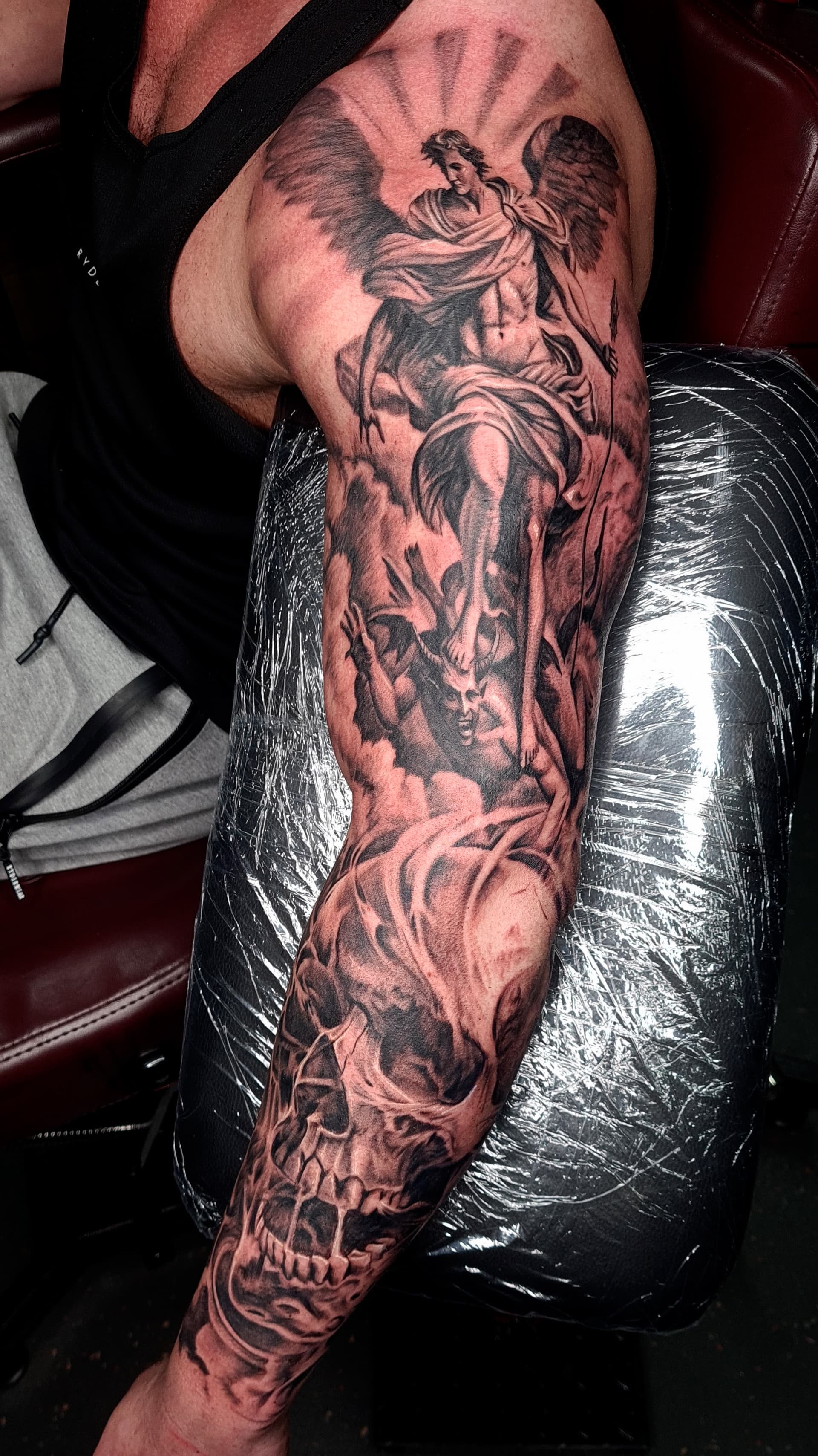 Detailed black and grey realism tattoo of an angel and a skull on an arm.