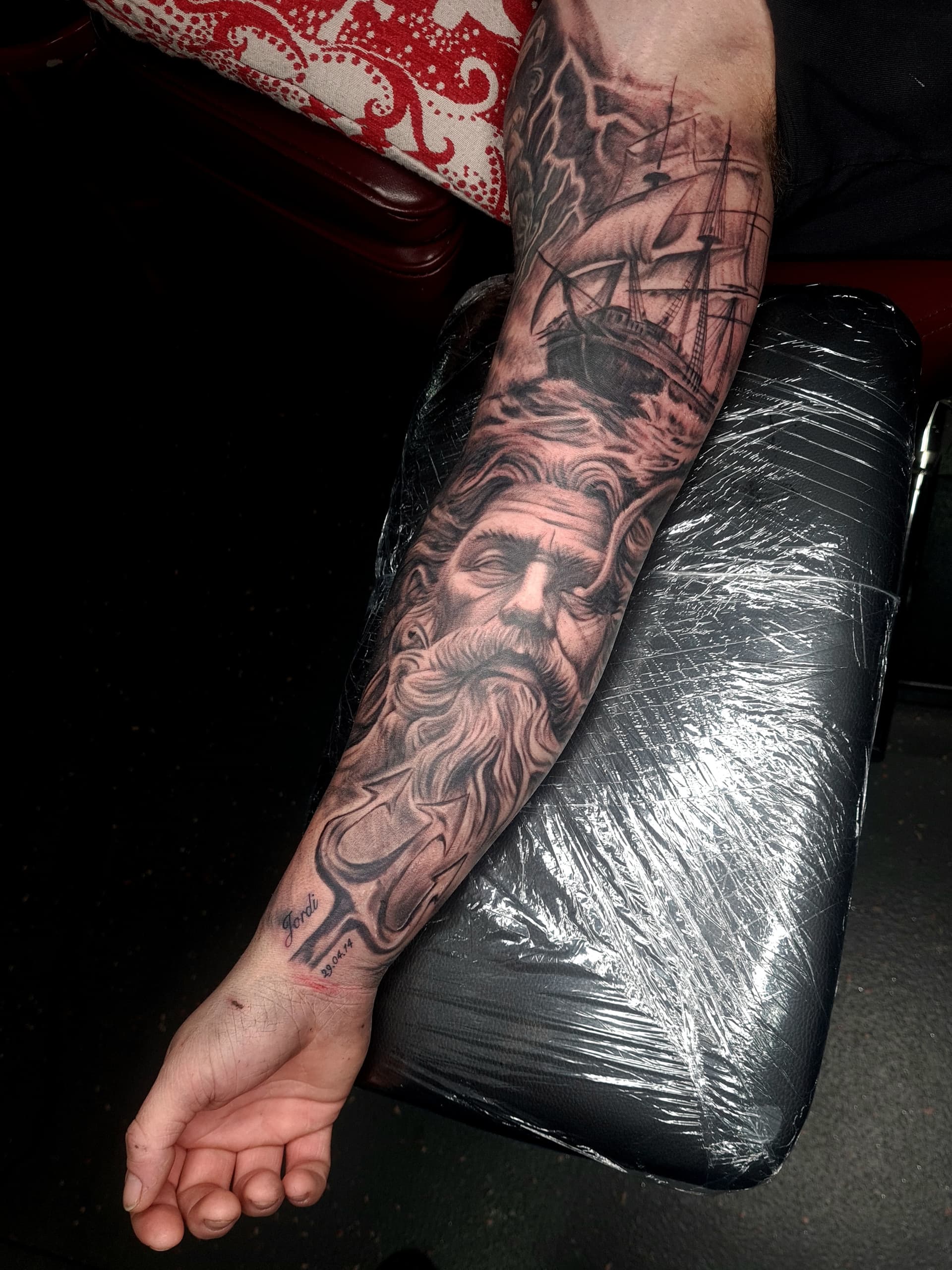 Tattoo featuring a detailed old sailor and ship in black and grey on arm.