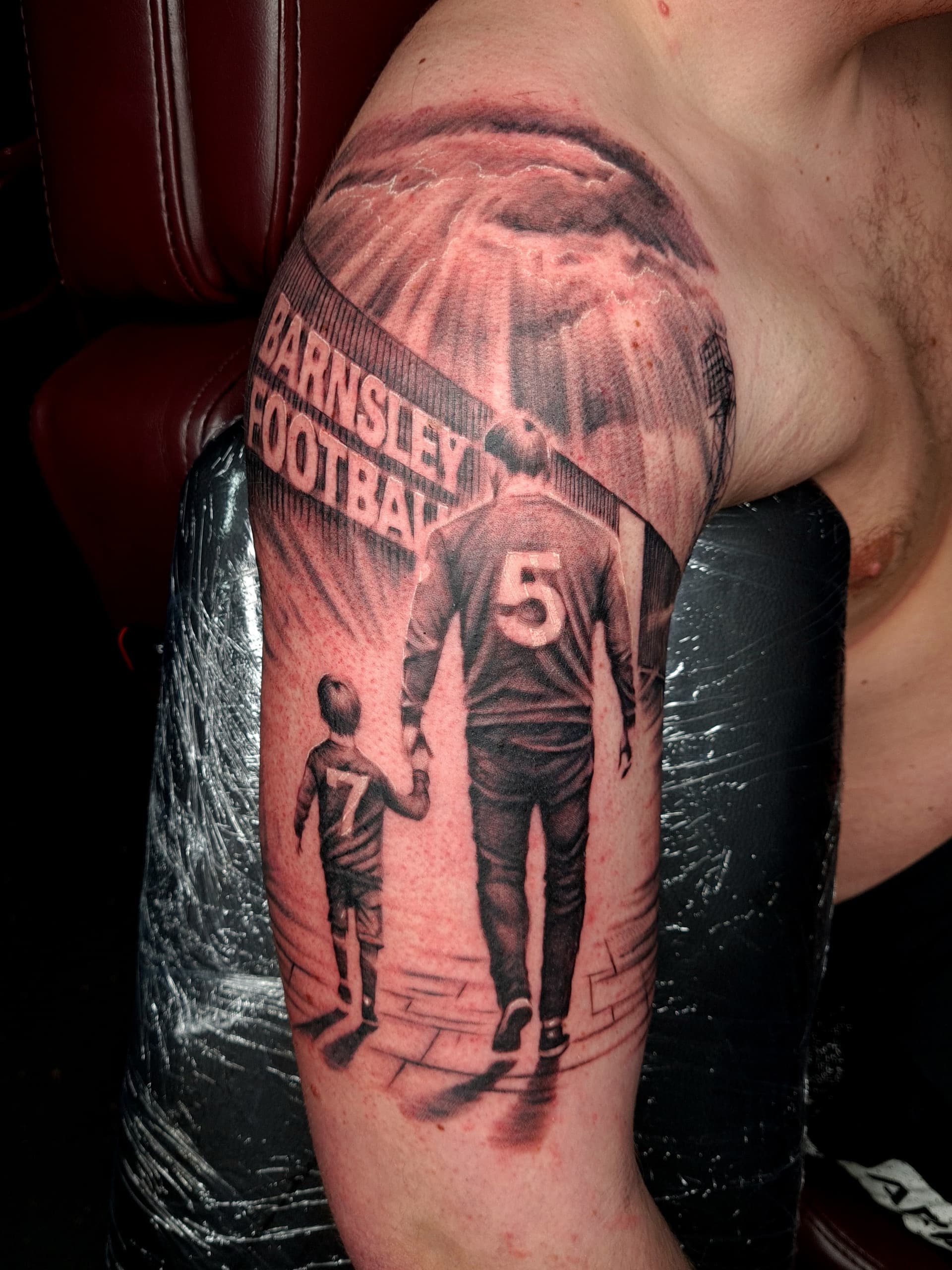 Realistic black and grey tattoo of a father and son walking, arm placement.