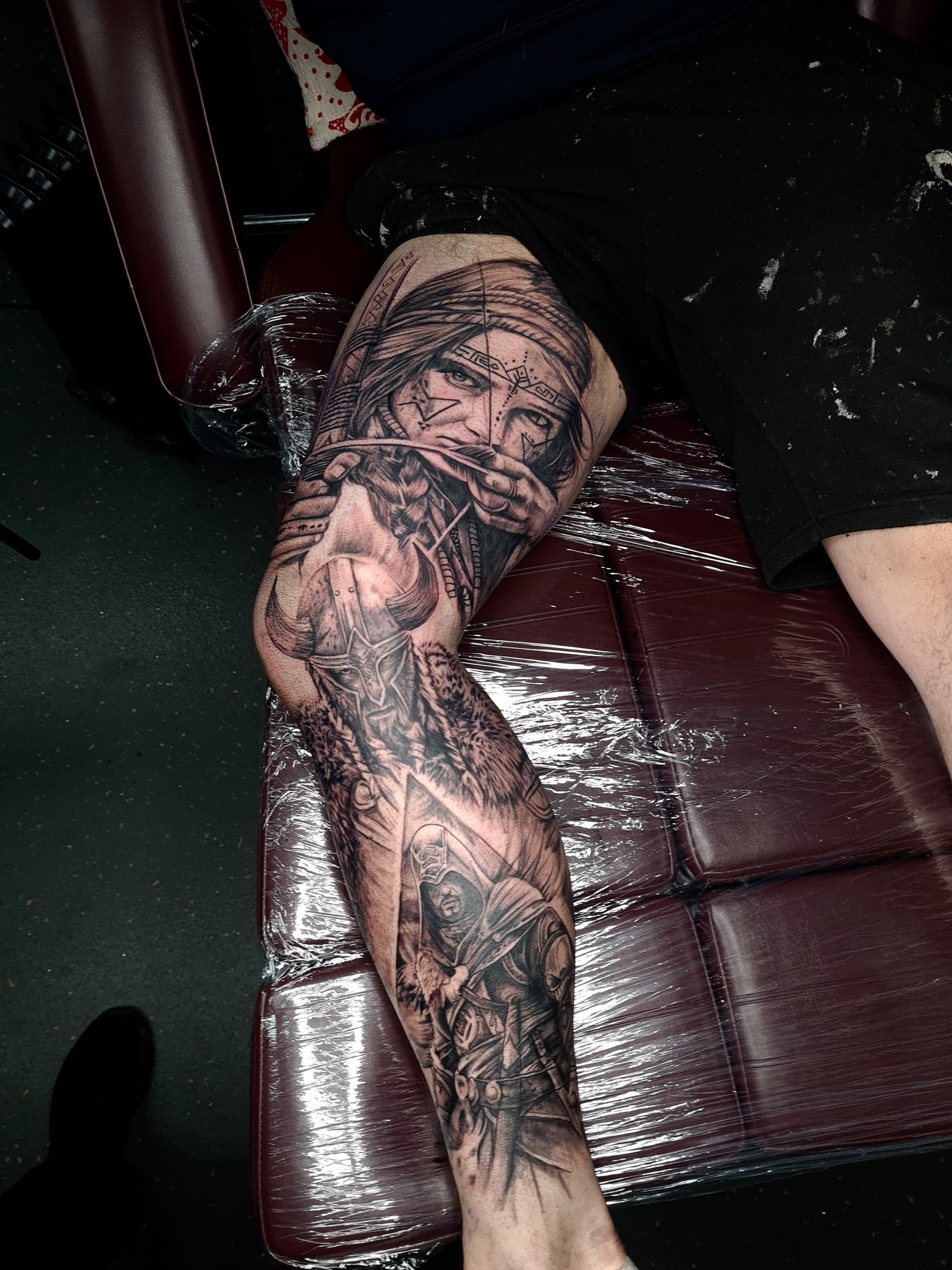 Detailed black and grey realism leg sleeve tattoo of a warrior and symbols.