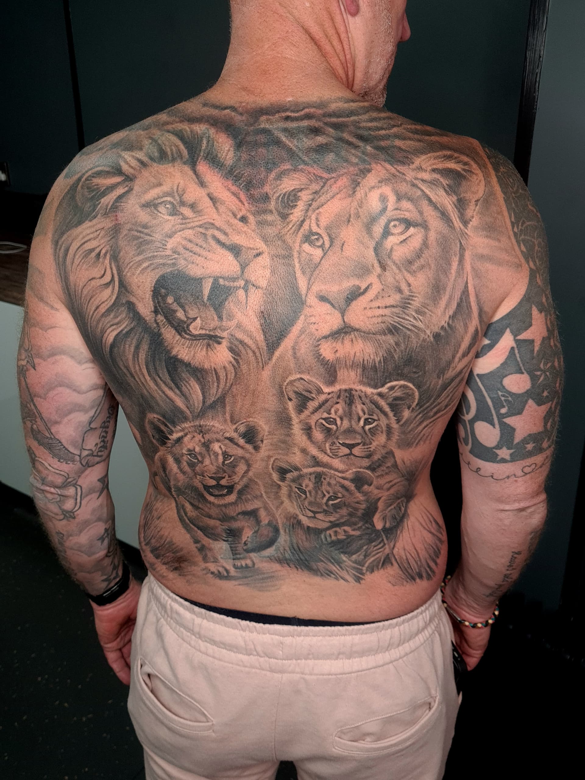 Detailed black and grey realism tattoo of lions and cubs on back.