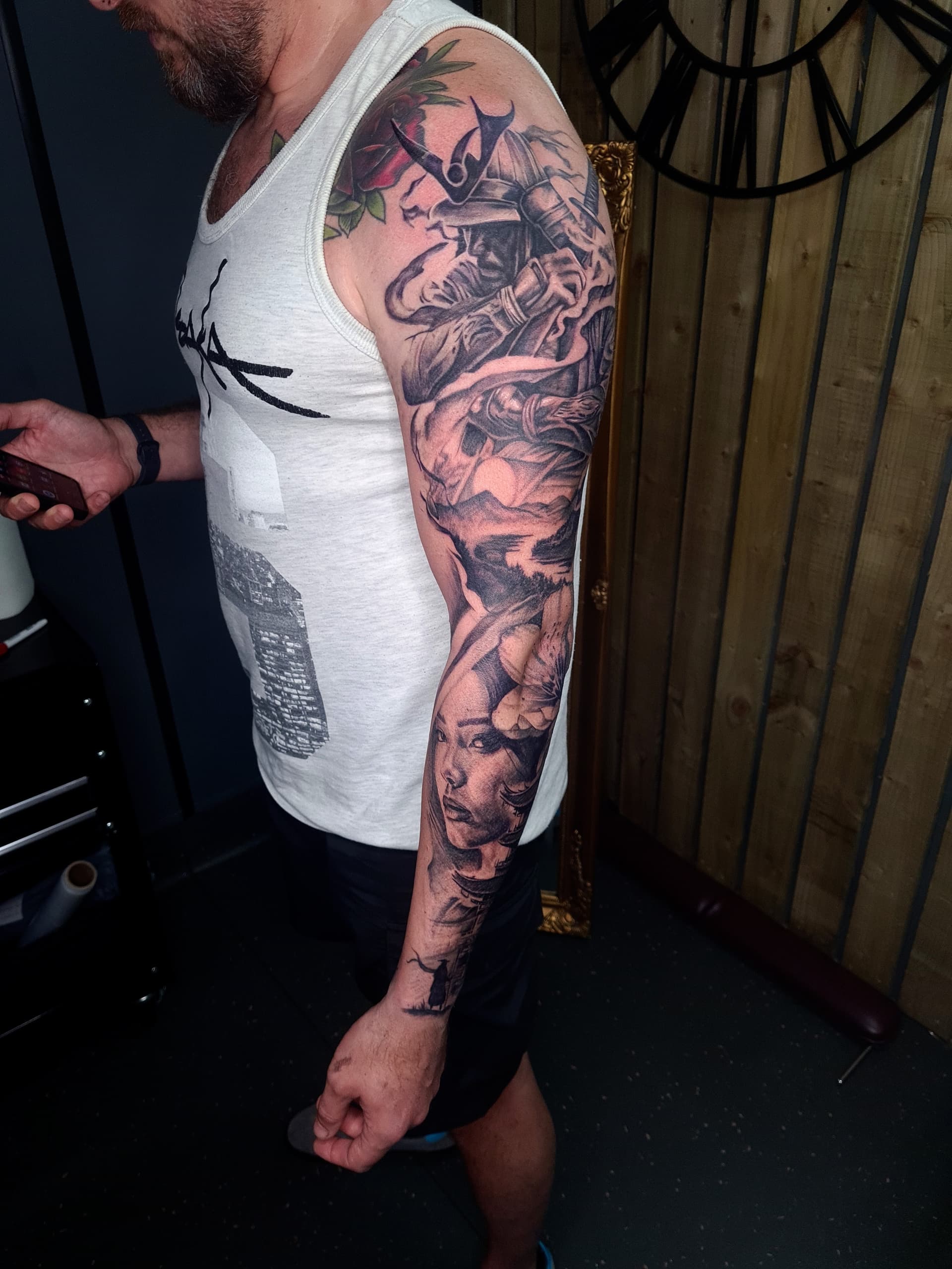 Detailed black and grey realism tattoo on arm, showcasing a samurai and a woman's portrait.