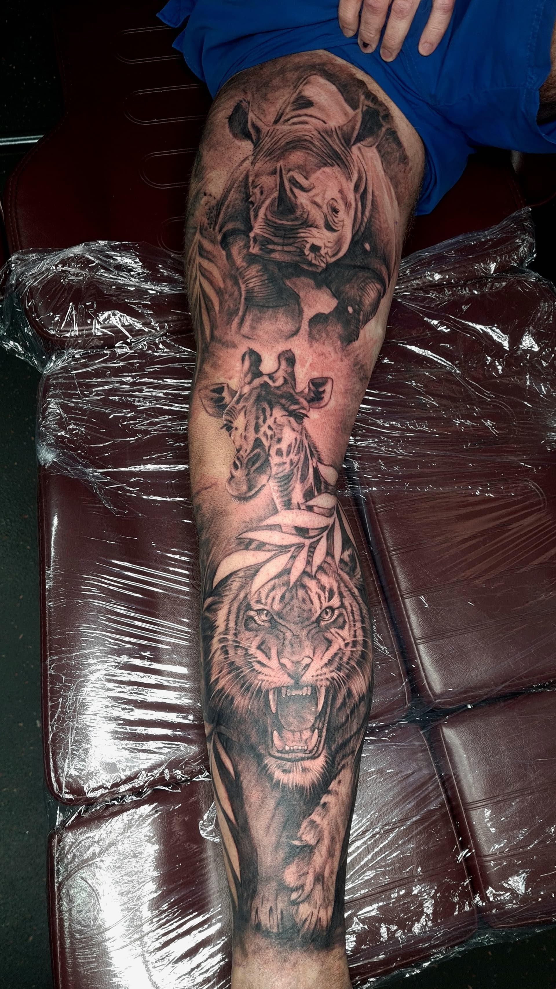 Realistic black and grey tattoo sleeve with tiger, giraffe, and rhino on leg.