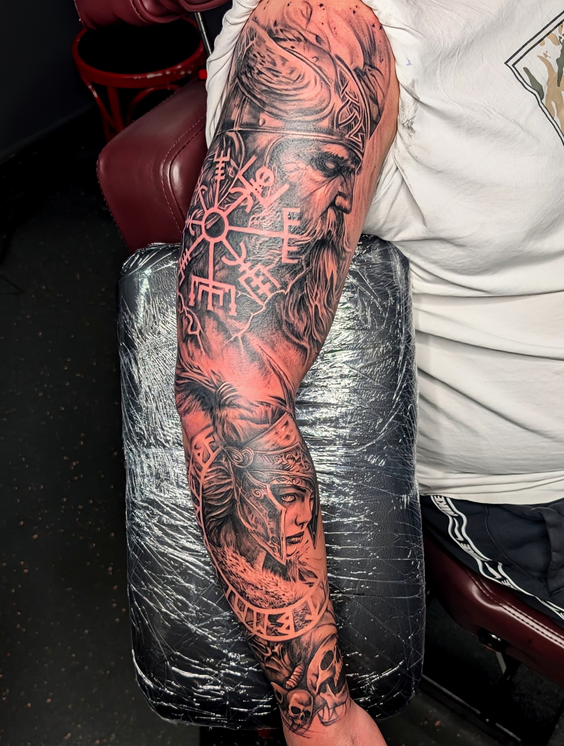 Black and grey realism tattoo of a warrior and symbols on arm sleeve.