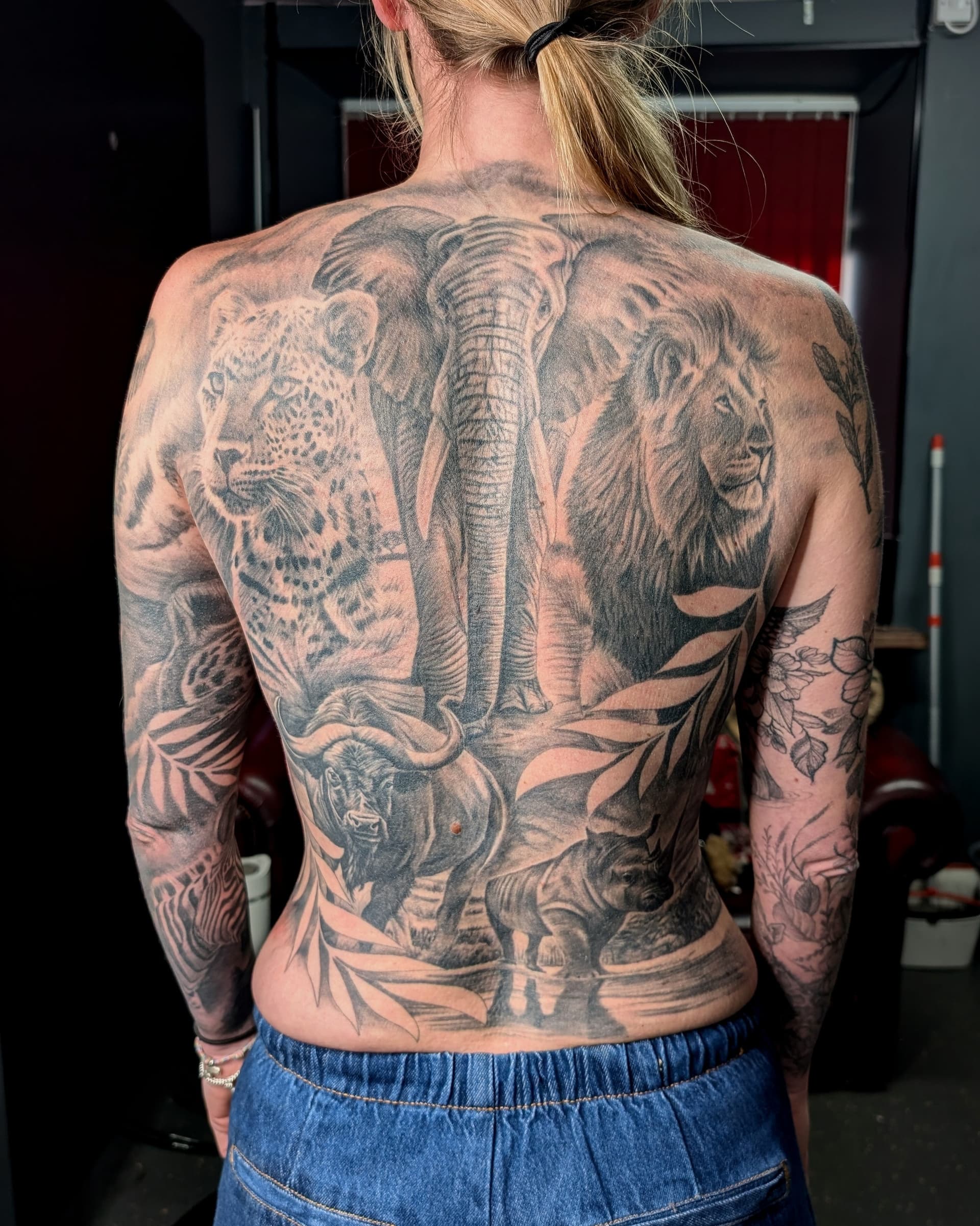 Detailed black grey realism tattoo featuring a lion, elephant, and leopard on back.