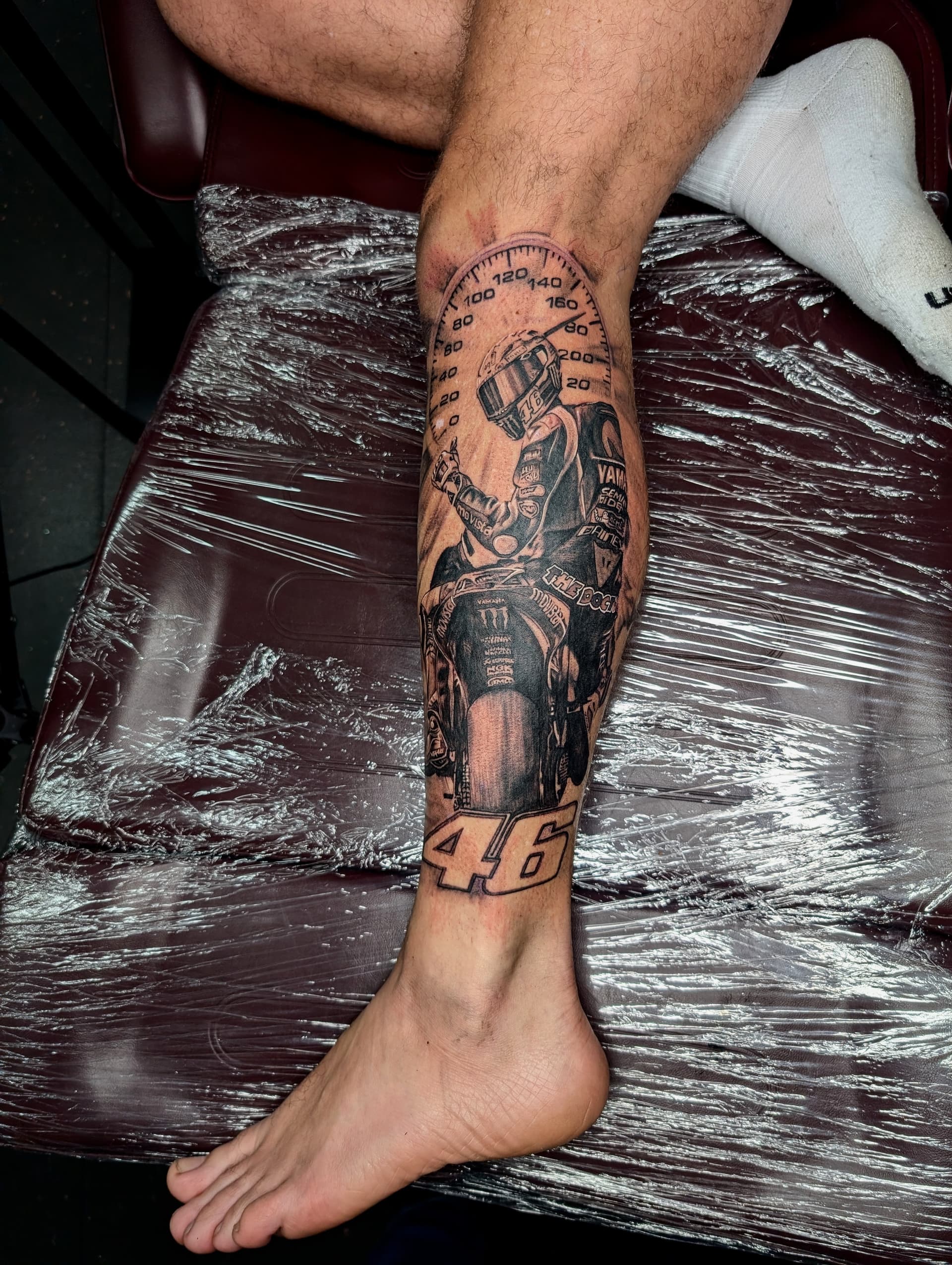Black and grey realism tattoo of a motorcyclist on leg with speedometer.