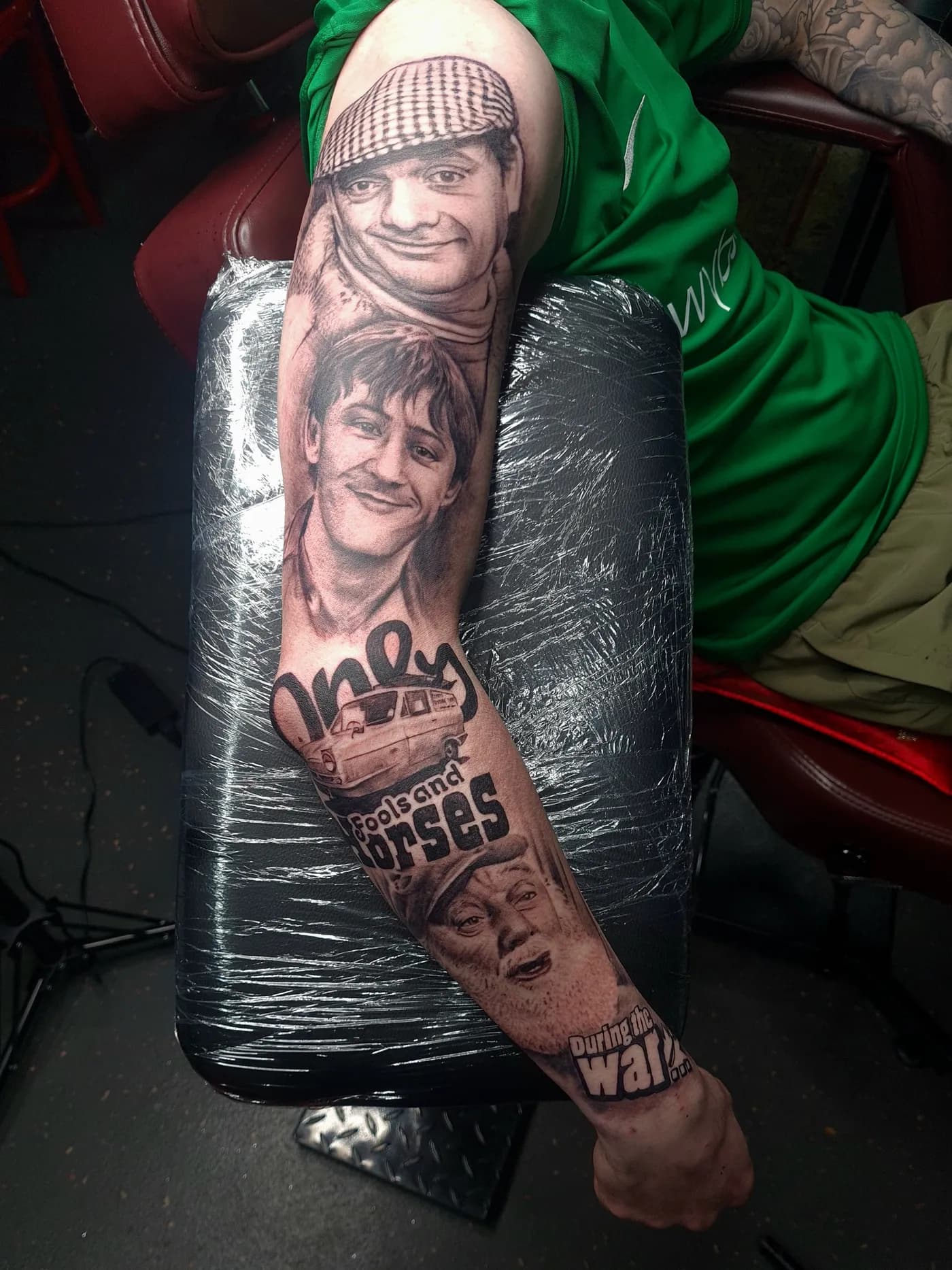 Only Fools and Horses tattoo sleeve, outer arm — black and grey realism portraits of Del Boy in his flat cap and Rodney, with the yellow Trotter Reliant van, the show's logo and Uncle Albert saying 'During the war', by Liam Rebel Tattoos Sheffield