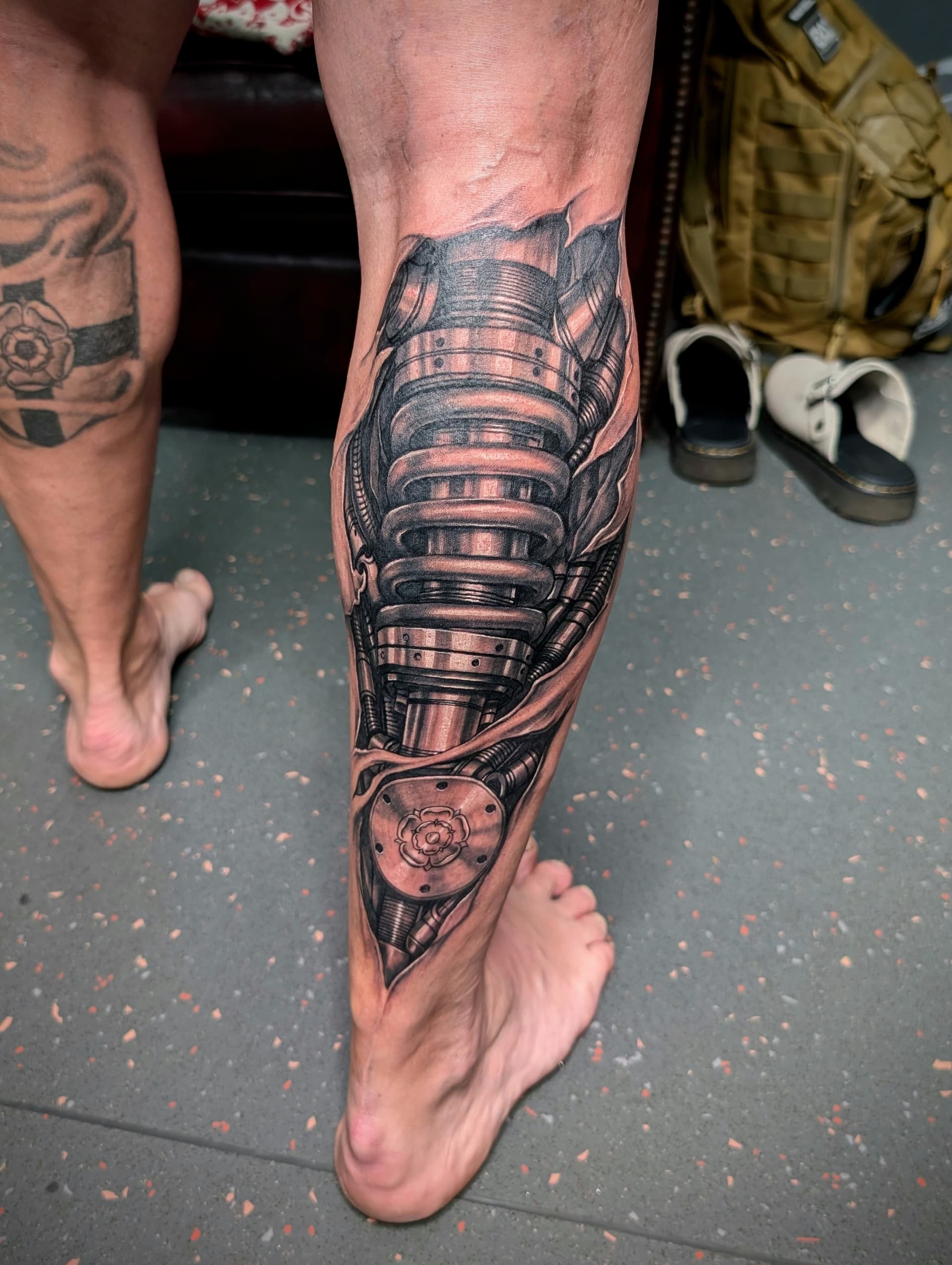 Black and grey realism tattoo of biomechanical machinery tearing through skin on the calf